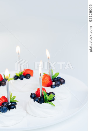 Meringue dessert Pavlova cake nests with fresh strawberries and blueberries with mint on the white plate with burning candles. Happy Birthday cake idea. Vertical card. Copy space. Selective focus Meringue dessert Pavlova cake nests with fresh strawberries and blueberries with mint on the white plate with burning candles. Happy Birthday cake idea. Vertical card. Copy space. Selective focus 93126066