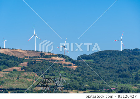 Panoramic view of wind farm or wind park, with turbines for generation electricity on sunny summer day. Green energy concept. Eco renewable energy power. 93126427