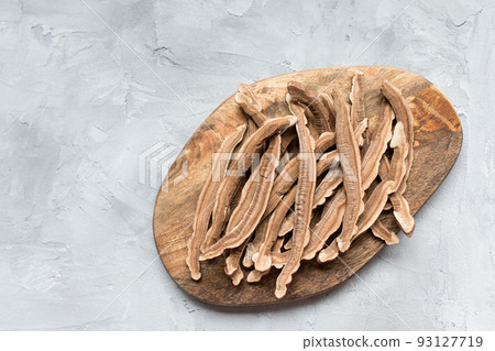 Slices of dried lingzhi mushroom, also called reishi or Ganoderma Lucidum, on a wooden board, gray background. Chinese traditional medicine product. Copy space. 93127719