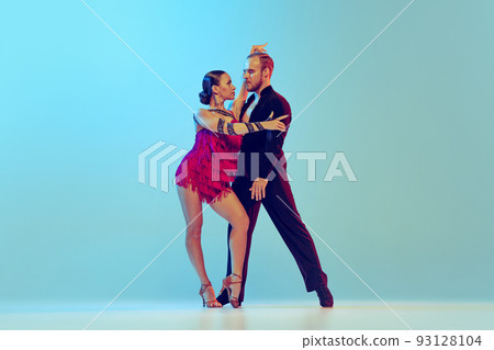 Studio shot of young couple, professional dancers dancing ballroom dance isolated on blue background. Concept of art, beauty, music, style. 93128104