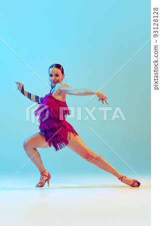 Fiery dance. Young graceful flexible woman dancing ballroom dance without partner isolated on blue background in neon light. Concept of art, beauty Fiery dance. Young graceful flexible woman dancing ballroom dance without partner isolated on blue background in neon light. Concept of art, beauty 93128128