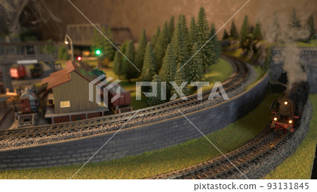 Steam locomotives running on model railroad. Passenger and freight trains speeding through miniature railway station. Steam locomotives running on model railroad. Passenger and freight trains speeding through miniature railway station. 93131845