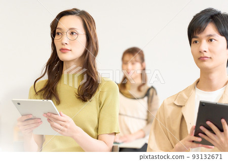 Young men and women taking a seminar while holding a tablet Young men and women taking a seminar while holding a tablet 93132671
