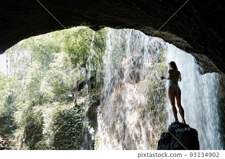 Woman sit on rock under waterfall in tropical jungle 93134902