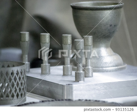 Object printed on metal 3d printer close-up. Object printed in laser sintering machine. Modern 3D printer printing from metal powder. Concept progressive additive DMLS, SLM, SLS 3d printing technology Object printed on metal 3d printer close-up. Object printed in laser sintering machine. Modern 3D printer printing from metal powder. Concept progressive additive DMLS, SLM, SLS 3d printing technology 93135126