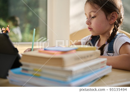 Adorable schoolgirl doing her homework with digital tablet at home. Child using gadgets to study. Education and distance learning for kids. Homeschooling during quarantine. Stay at home entertainment. Adorable schoolgirl doing her homework with digital tablet at home. Child using gadgets to study. Education and distance learning for kids. Homeschooling during quarantine. Stay at home entertainment. 93135494