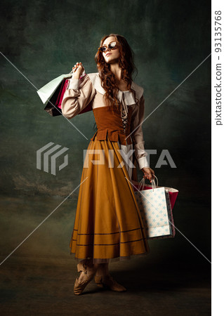 Eras comparison. Young atractive redhair girl with long curly hair like girl of renaissance eras isolated on dark background. Shopping, beauty, art, black friday Eras comparison. Young atractive redhair girl with long curly hair like girl of renaissance eras isolated on dark background. Shopping, beauty, art, black friday 93135768