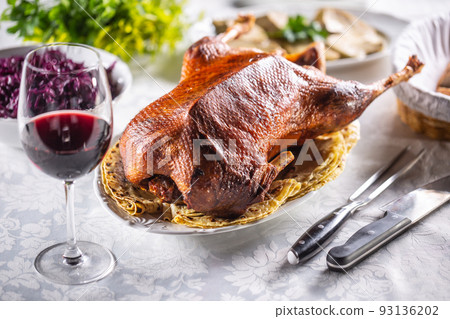Roast goose with side dishes, red cabbage, roast, strudel, potato dumplings, pickles, bread and red wine. Traditional holiday food 93136202