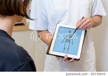 A scene of explaining to a patient with a human skeleton model on a tablet screen at an osteopathic clinic, a chiropractic clinic, an orthopedic clinic, or a clinic 93136643
