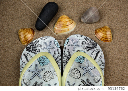 Old Flip Flop Sandals with Sea Shells and Stones on a Coastal Beach Old Flip Flop Sandals with Sea Shells and Stones on a Coastal Beach 93136762