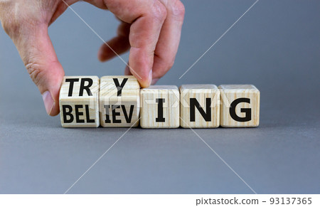 Trying and believing symbol. Businessman turns wooden cubes and changes the word Believing to Trying. Beautiful grey table grey background, copy space. Business, trying and believing concept. 93137365