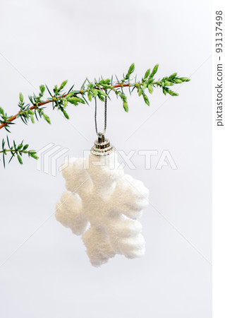 Soft selective focus on white snowflake Christmas toy hanging on green branch of Christmas tree, juniper on white background. Minimal style. Happy holidays. Vertical Photo. Copy space Soft selective focus on white snowflake Christmas toy hanging on green branch of Christmas tree, juniper on white background. Minimal style. Happy holidays. Vertical Photo. Copy space 93137498