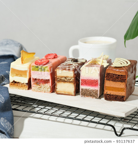 mini cakes with various fillings layered. cut cakes on a wooden board with fruit and chocolate decor. sweet dessert for wedding or birthday table, summer delisious treats. mini cakes with various fillings layered. cut cakes on a wooden board with fruit and chocolate decor. sweet dessert for wedding or birthday table, summer delisious treats. 93137637