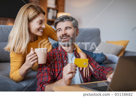 Smiling adult european woman with cup of drink hug man with laptop and credit card, enjoy shopping online Smiling adult european woman with cup of drink hug man with laptop and credit card, enjoy shopping online 93138682