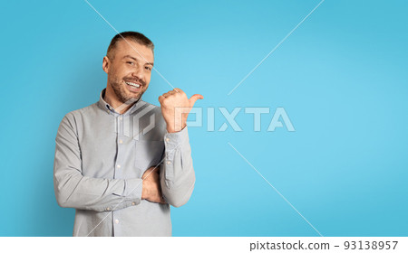 Cheerful Mature Man Pointing Thumb Finger Aside Over Blue Background 93138957