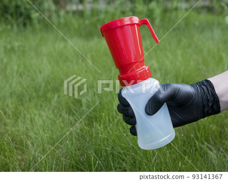 Hand in black nitrile glove holding a teat dip cup for udder cow disinfection on green grass background, copy space. Milking practice 93141367