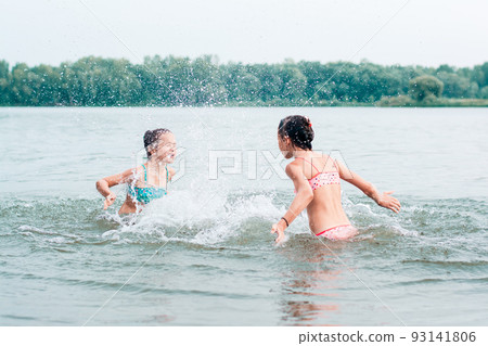 Two cheerful girls splash each other with water in the river. Local tourism. Summer vacation Two cheerful girls splash each other with water in the river. Local tourism. Summer vacation 93141806