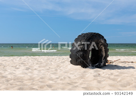 A large tyre, abandoned by the shore of a beautiful beach. The environmental problem with plastic A large tyre, abandoned by the shore of a beautiful beach. The environmental problem with plastic 93142149