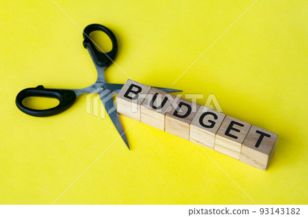 Scissor cutting wooden blocks with text BUDGET. Cutting budget concept. Scissor cutting wooden blocks with text BUDGET. Cutting budget concept. 93143182