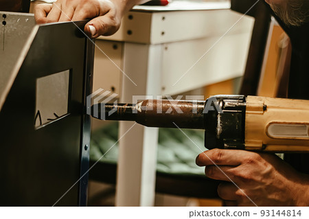 Male worker uses electric riveting gun. Hand holding  riveting m 93144814