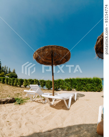 Couple of deck chairs with a straw parasol and some plants Couple of deck chairs with a straw parasol and some plants 93154774