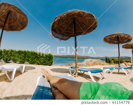 Point of view of a tourist on deck chairs with straw parasols near the river Point of view of a tourist on deck chairs with straw parasols near the river 93154776