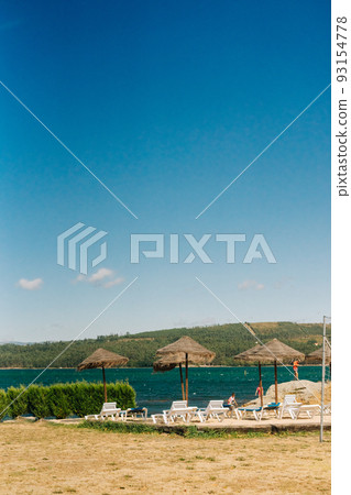 Natural solarium with deck chairs and straw parasols near the river 93154778