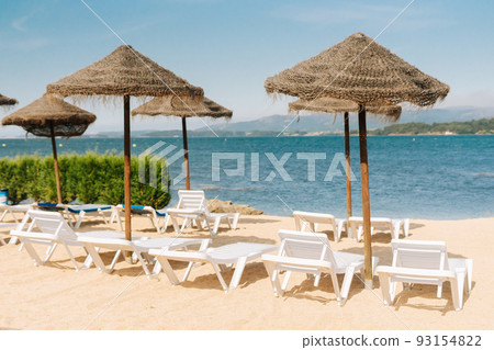 Deck chairs with straw parasols near the river Deck chairs with straw parasols near the river 93154822