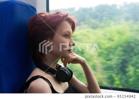girl rides on a commuter train and looks out the window at a natural landscape blurred in motion girl rides on a commuter train and looks out the window at a natural landscape blurred in motion 93154942