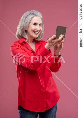 Mature woman in red doing makeup and looking contented 93155030