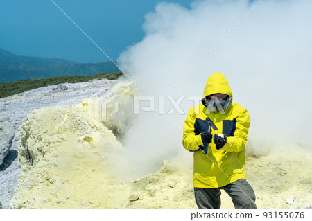 man volcano scientist on the background of a smoking fumarole examines a sample of a sulfur mineral with a geological hammer man volcano scientist on the background of a smoking fumarole examines a sample of a sulfur mineral with a geological hammer 93155076
