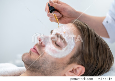 Professional cosmetologist applying hydrating mask on mans eye area Professional cosmetologist applying hydrating mask on mans eye area 93155216