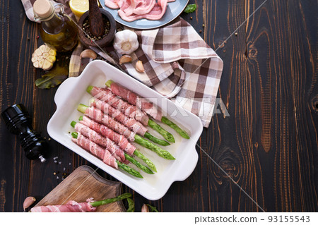 ceramic baking dish with aspargus covered with bacon on wooden kitchen table 93155543