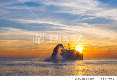 Vessel engaged in dredging at sunset time. Hopper dredger working at sea. Ship excavating material from a water environment. Beautiful sunset, Baltic sea 93158665