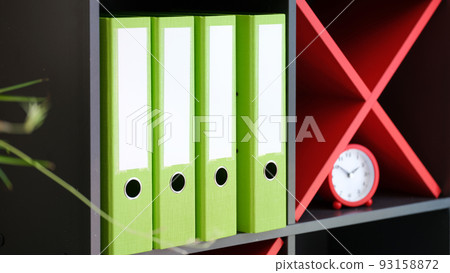 Shelves with office folders with documents and red alarm-clock Shelves with office folders with documents and red alarm-clock 93158872