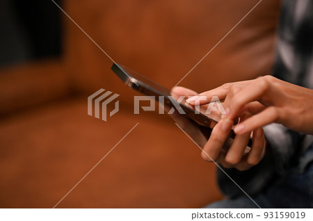 A female hands holding a smartphone over blurred modern living room in the background. A female hands holding a smartphone over blurred modern living room in the background. 93159019