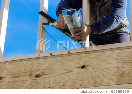 In this case, the builder uses an air hammer when nailing wooden beams for construction in the housing development. In this case, the builder uses an air hammer when nailing wooden beams for construction in the housing development. 93160189