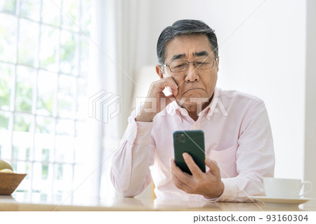 Senior man thinking while looking at smartphone Senior man thinking while looking at smartphone 93160304