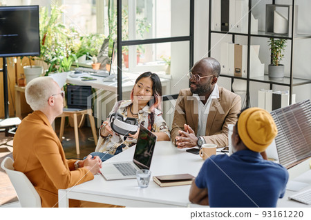 Group of programmers sitting at table and discussing together new app of VR glasses during meeting at office 93161220