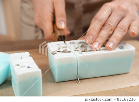 Woman cutting natural handmade soap on wooden table, closeup Woman cutting natural handmade soap on wooden table, closeup 93162236