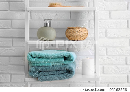 Clean soft towels and soap dispenser on shelves near white brick wall Clean soft towels and soap dispenser on shelves near white brick wall 93162258