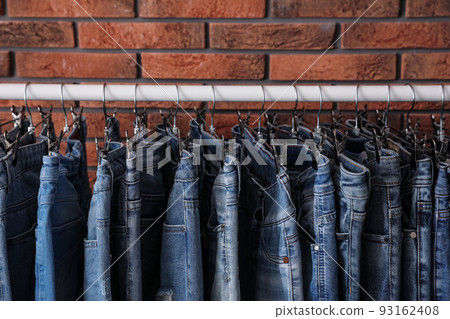 Rack with stylish jeans near brick wall, closeup Rack with stylish jeans near brick wall, closeup 93162408