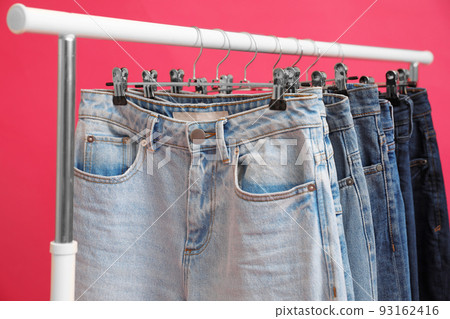 Rack with stylish jeans on pink background, closeup 93162416