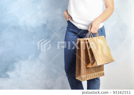 Woman with gold shopping paper bags on light blue background, closeup. Space for text 93162551