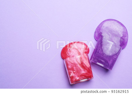 Overturned plastic containers with bright slimes on violet background, top view. Space for text 93162915