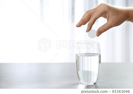 Woman putting tablet into glass of water indoors, space for text Woman putting tablet into glass of water indoors, space for text 93163046
