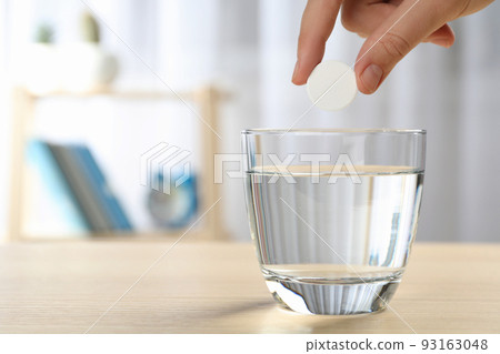 Woman putting tablet into glass of water indoors, space for text Woman putting tablet into glass of water indoors, space for text 93163048