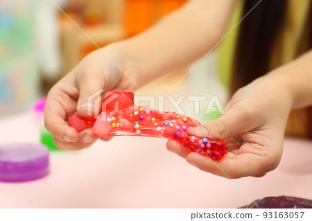Little girl playing with red slime indoors, closeup Little girl playing with red slime indoors, closeup 93163057