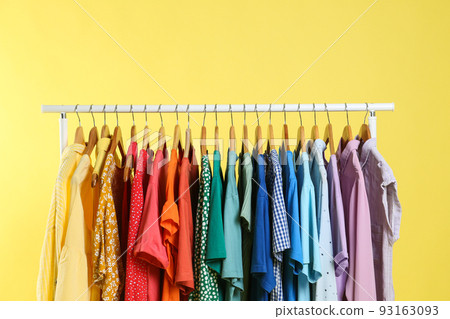 Bright clothes hanging on rack against yellow background. Rainbow colors 93163093