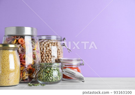 Jars with different cereals on white wooden table against violet background. Space for text 93163100